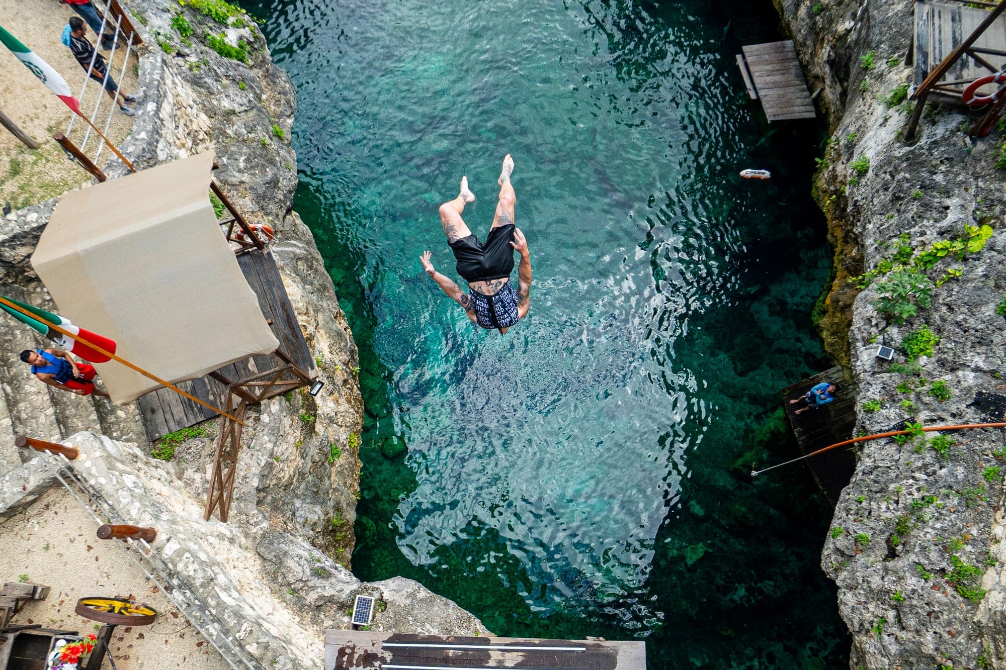 Looking straight down at a jumper about to hit the turquoise water of a cenote