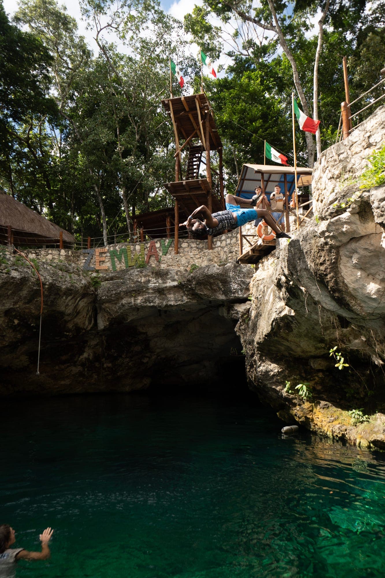 A jumper leaping from a rock ledge beneath a cenote cave overhang