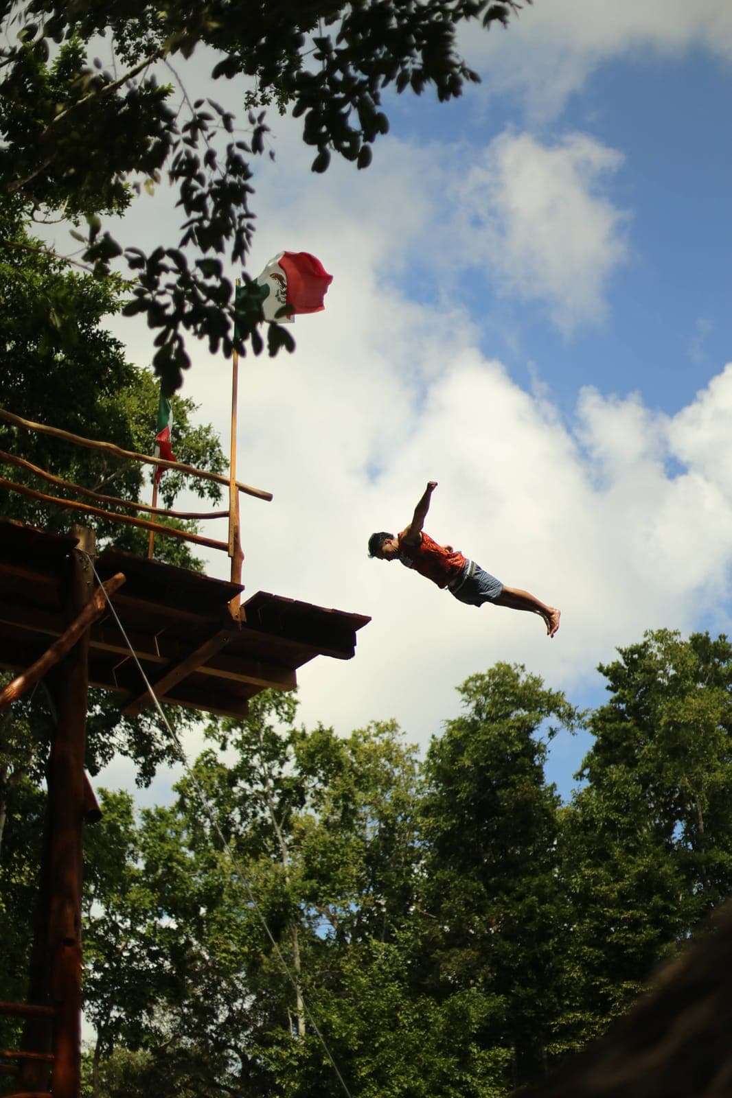 A jumper mid-air against the clouds, high above the cenote